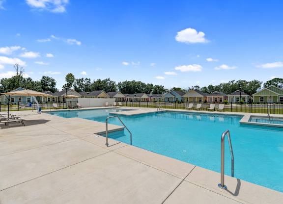 A large swimming pool surrounded by a concrete patio and lounge chairs.