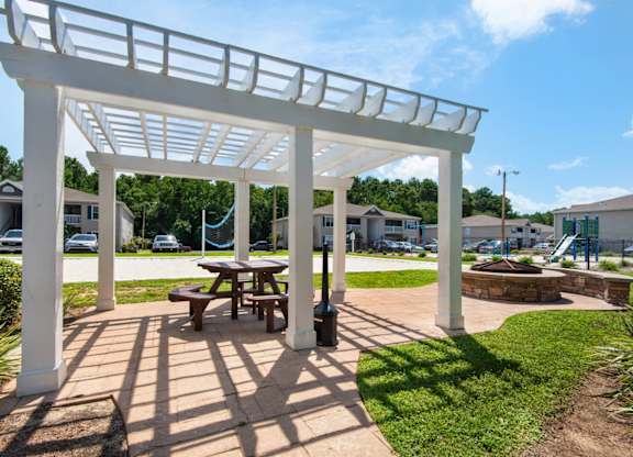 A white pergola with a picnic table underneath it and a fire place to the side at Crystal Lake in Pensacola, Florida.