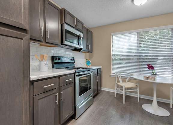 A kitchen with brown cabinets, stainless-steel appliances, granite countertops, and a white tile backsplash at Crystal Lake in Pensacola, Florida.