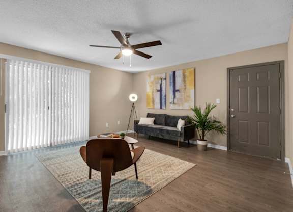 A furnished living room with a sliding door, ceiling fan, and wood flooring at Crystal Lake in Pensacola, Florida.