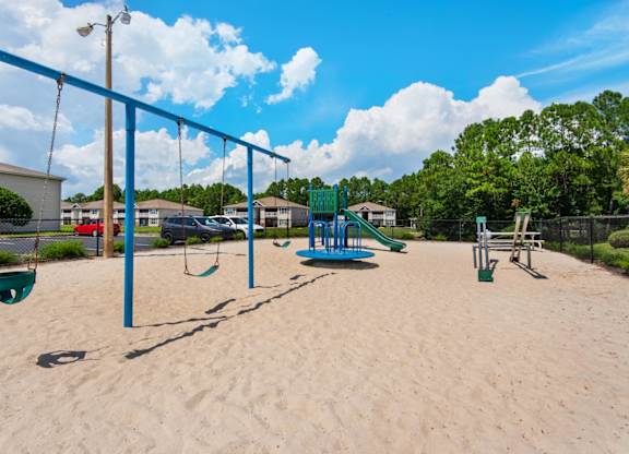 A playground with swings, a slide, and a seesaw at Crystal Lake Apartments in Pensacola, FL.