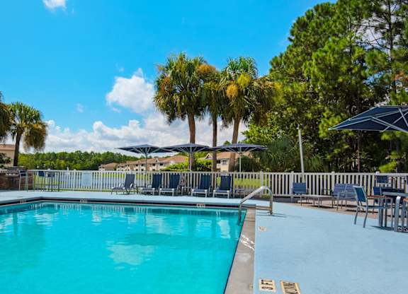 A large, gated, swimming pool with ladder access surrounded by palm trees and lounge chairs at Crystal Lake in Pensacola, Florida.