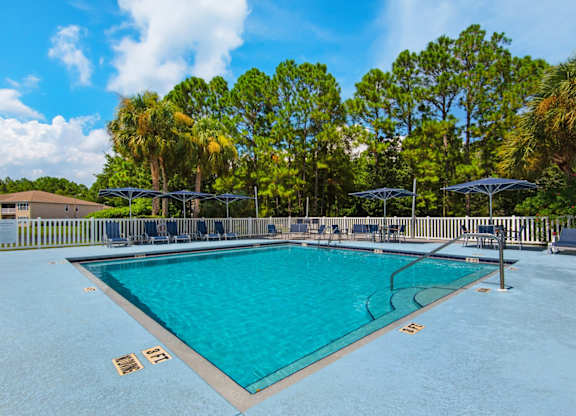 An outdoor swimming pool surrounded by trees and umbrellas at Crystal Lake in Pensacola, Florida.