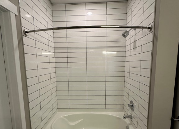 A white tiled shower with a white tub  at The Fitzroy Apartments in Birmingham, AL
