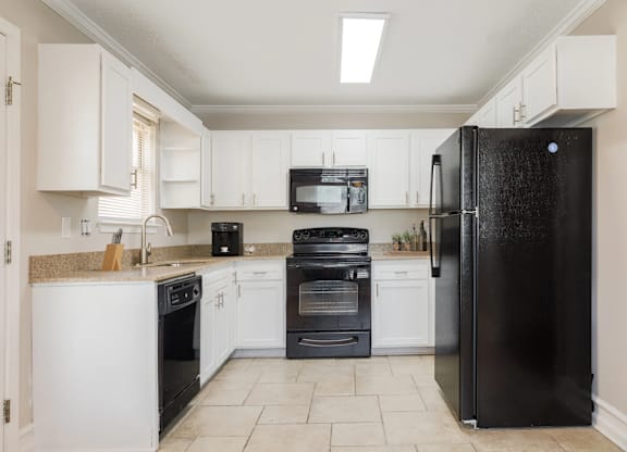 A black refrigerator stands in a kitchen with white cabinets and appliances.