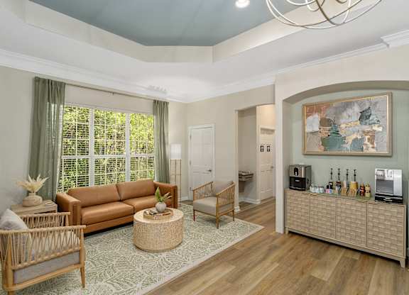 A living room with a brown sofa, a wooden chair, a wicker table, and a painting on the wall.