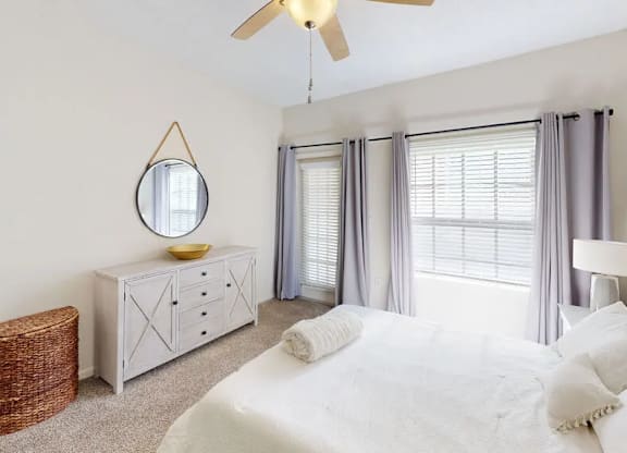 A bedroom with a white bed, a white dresser, and a white ceiling fan.
