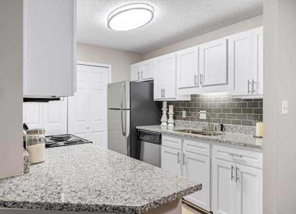 A kitchen with granite countertops, white cabinets, and a laundry closet at Summerchase at Riverchase in Hoover, Alabama.