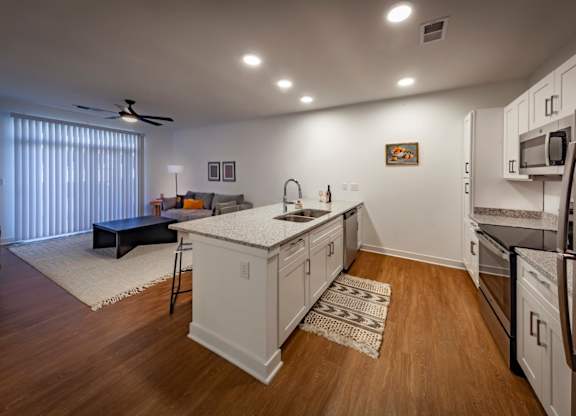 A kitchen with white cabinets, stainless steel appliances, wood-look flooring which opens into living room at Wesley Place Apartments in Indianapolis, IN