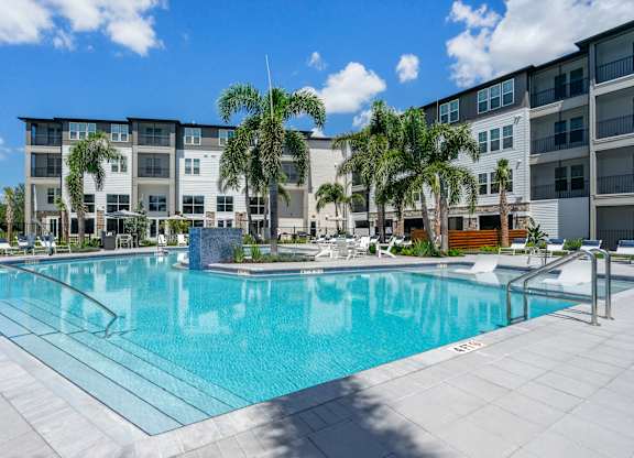 A large swimming pool in front of a building with palm trees.