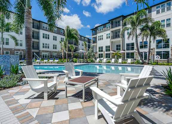 A pool surrounded by chairs and palm trees.