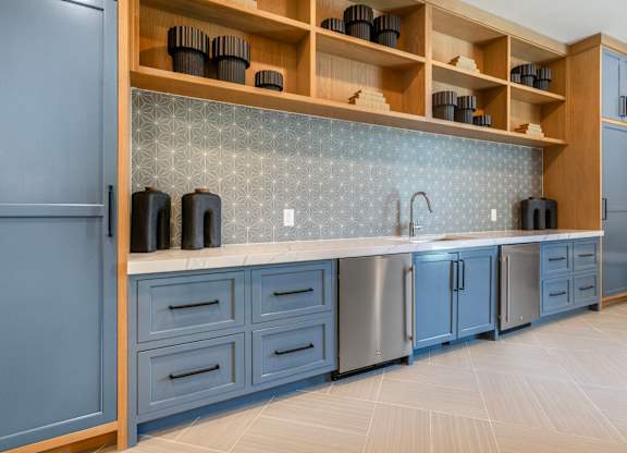 A kitchen with blue cabinets and a wooden shelf above the counter.