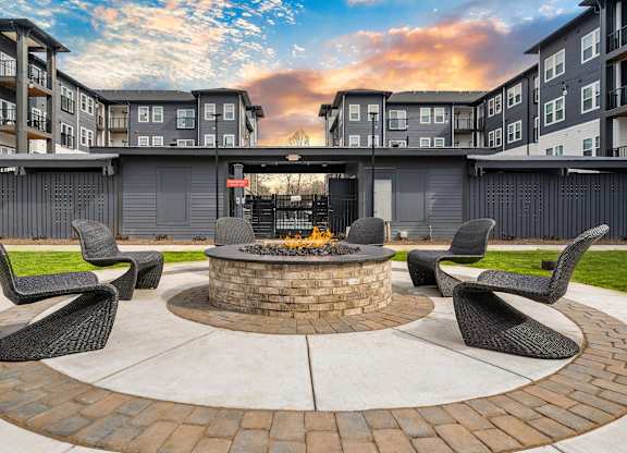 A fire pit sits in the middle of a brick patio surrounded by four chairs.