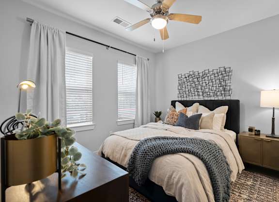 A bedroom with a bed, a ceiling fan, and a plant on a table.
