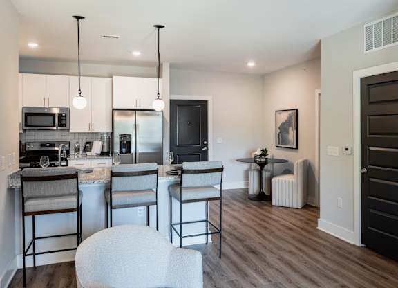 A modern kitchen with white chairs and a black door.