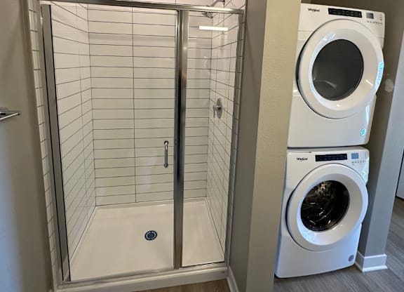 A white tiled shower area with a glass door and a washer and dryer at The Fitzroy Apartments in Birmingham, AL