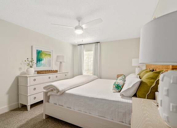 A white bedroom with a bed, nightstand, and a ceiling fan.