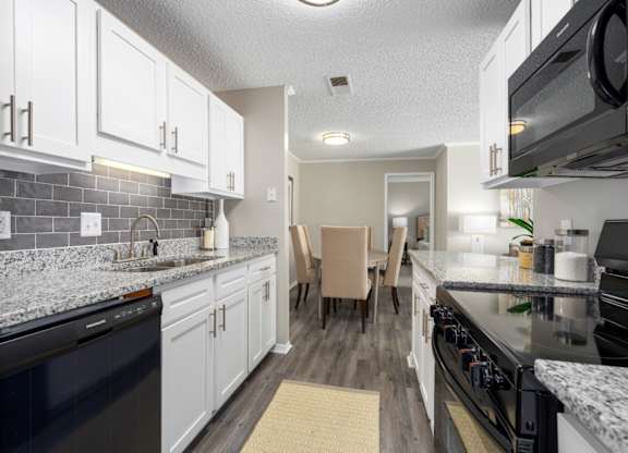 A kitchen with black appliances, granite countertops, white cabinets, and tile backsplash at Summerchase at Riverchase in Hoover, Alabama.