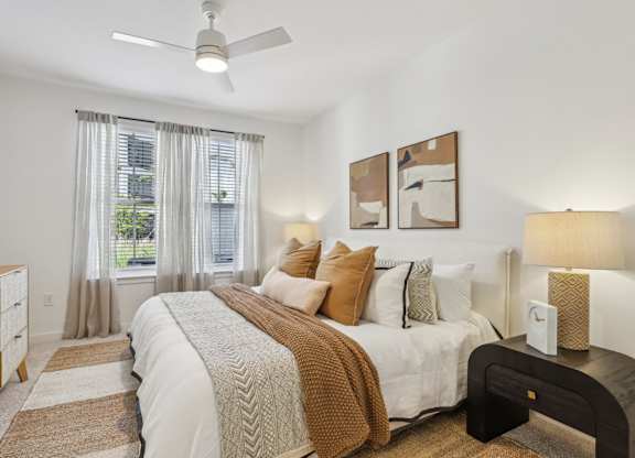 A bedroom with a large bed, a ceiling fan, and a window with curtains.