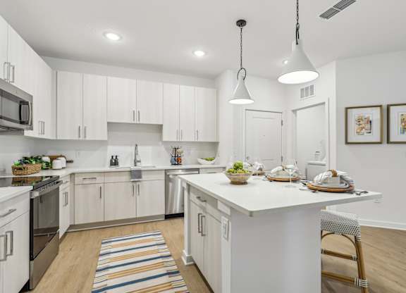 A kitchen with white cabinets and a white island with a bowl of fruit on it.