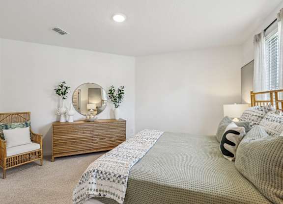 A bedroom with a bed, chair, and mirror.