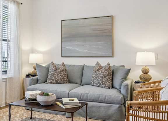 A living room with a grey couch, a coffee table, and a painting on the wall.