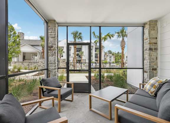 A patio with a couch, chair, and table with a view of a house and trees.