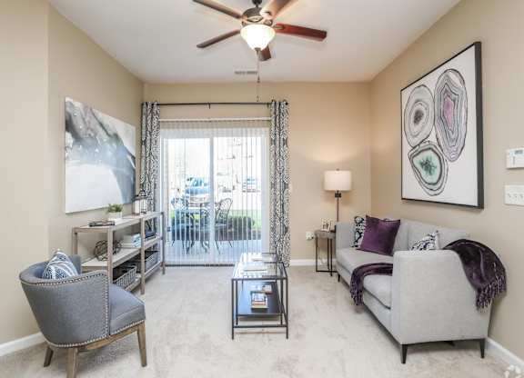 A living room with a grey couch, a chair, a coffee table, and a ceiling fan.
