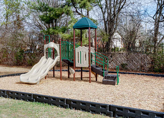 A playground with a green roof, a slide, a wooden swing set, and a sandbox.