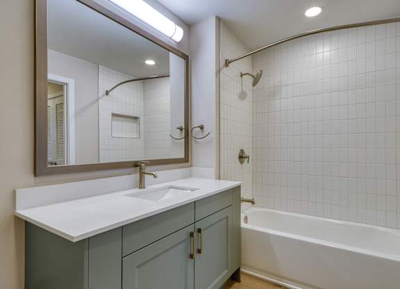 A white sink with a silver faucet and a white bathtub in a bathroom.
