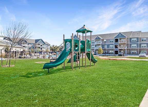 A green slide in a playground with apartment buildings in the background.