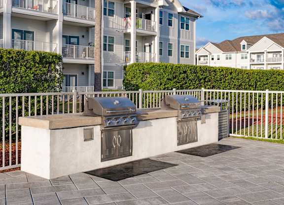 A white fence surrounds a fire pit in front of apartment buildings.