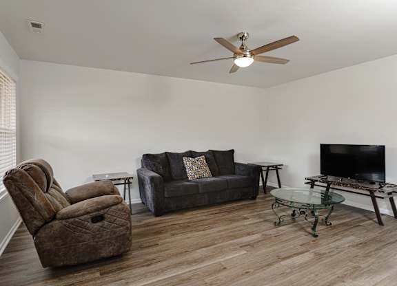 A living room with a brown chair, grey couch, and a glass coffee table.