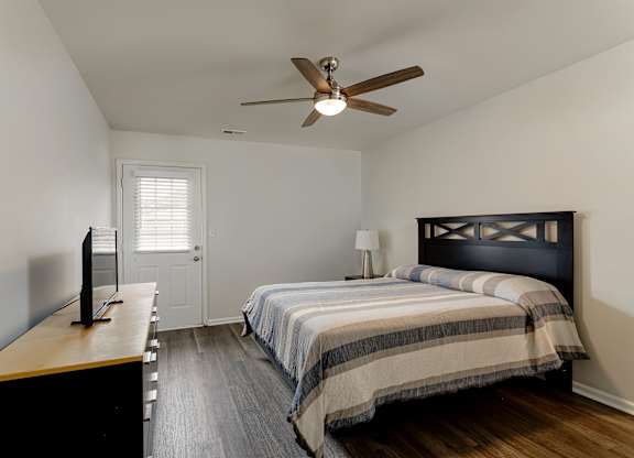 A bedroom with a bed, a television, and a ceiling fan.