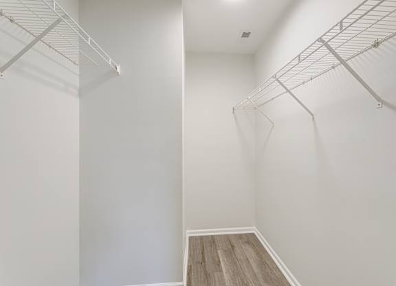 A walk in closet with white walls and wood flooring.