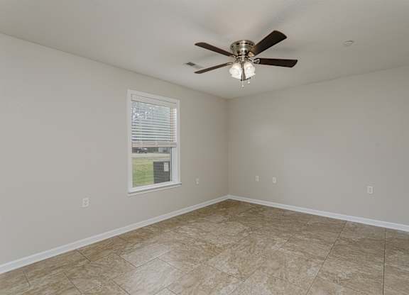 A room with a ceiling fan and a window showing a view of a lawn and a house.
