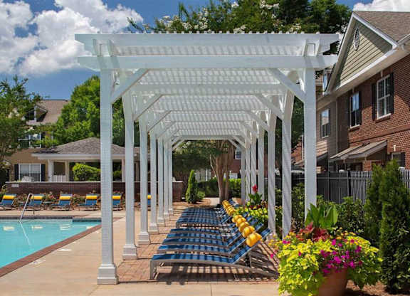 A white pergola is over a pool with blue chairs.