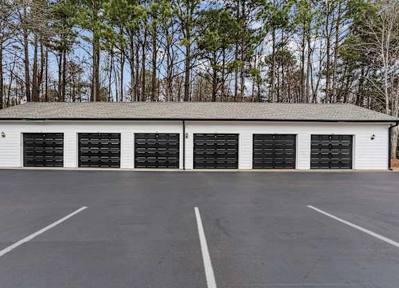 A large white building with black garage doors in the middle of a parking lot.