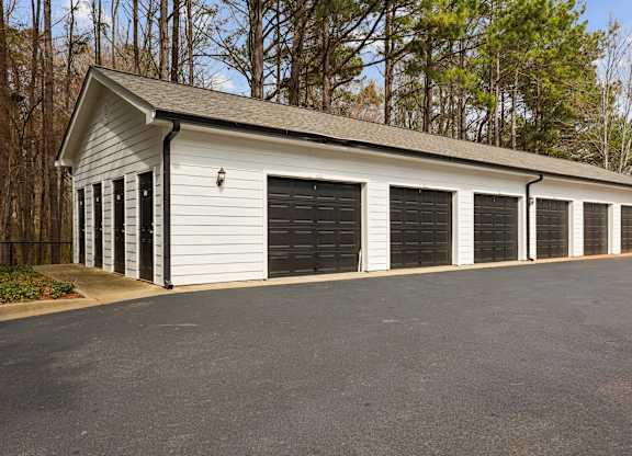 A white building with black garage doors sits in a parking lot.
