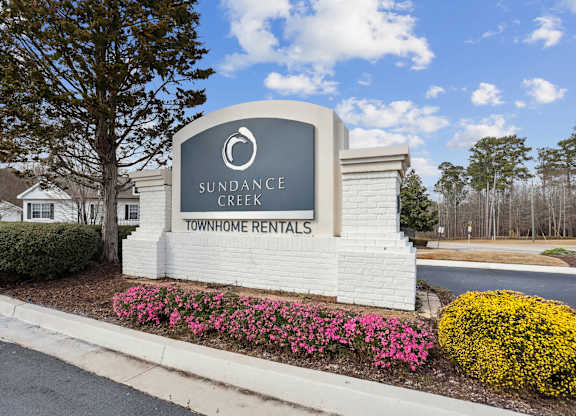 A sign for Sundance Creek Townhome Rentals is surrounded by flowers and greenery.