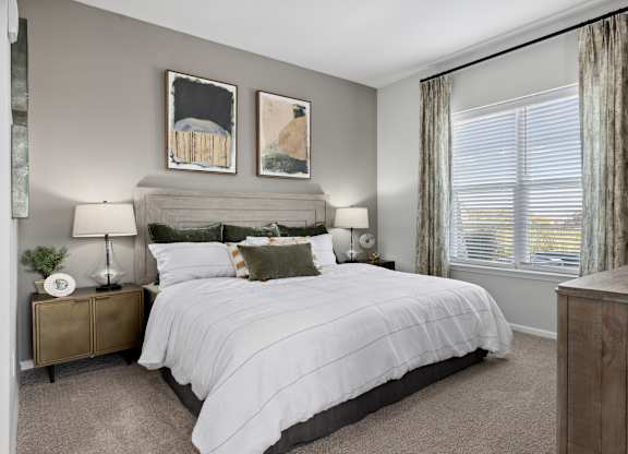 A bedroom with a large bed, two lamps, and two pictures on the wall.