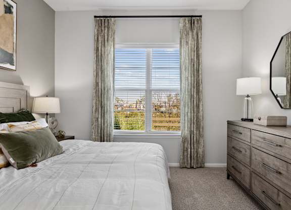 A well-lit bedroom with a large bed and a dresser with a mirror.