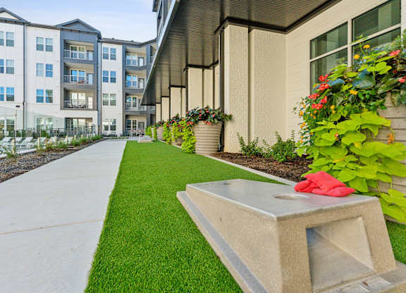 a sidewalk in front of an apartment building with grass and flowers
