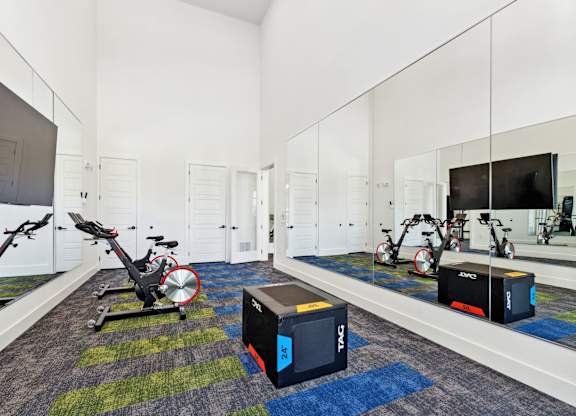 a gym with exercise equipment and a tv in a room with mirrored walls