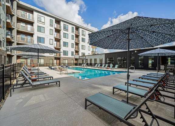 A pool area with sun loungers and a building in the background.