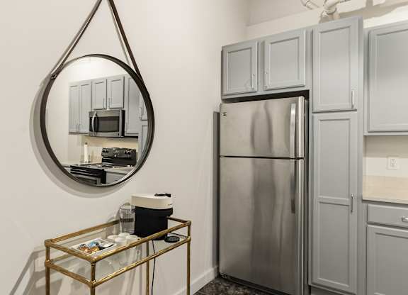 A modern kitchen with a stainless steel refrigerator and a round mirror above a coffee table at The Tower Apartments, Alabama, 35401