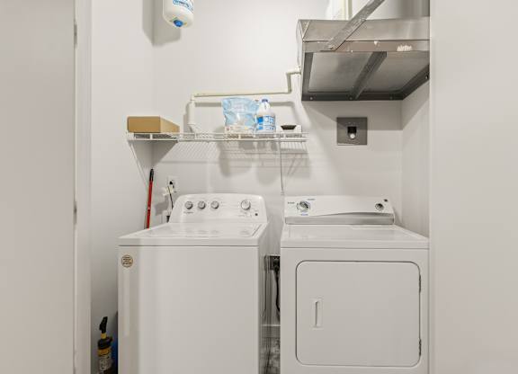 A white washing machine and dryer in a small laundry room at The Tower Apartments, Alabama, 35401