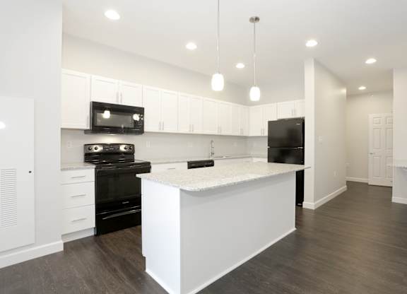 A modern kitchen with a white island and black appliances at Promenade at Founders Square Apartments in Indianapolis, IN
