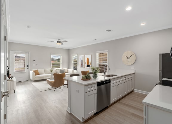 an open kitchen and living room with a large clock on the wall at The Cottages at Foley Farms apartments in Foley, AL