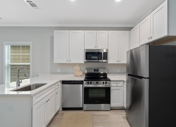 an all white kitchen with stainless steel appliances and white cabinets at The Cottages at Foley Farms apartments in Foley, AL